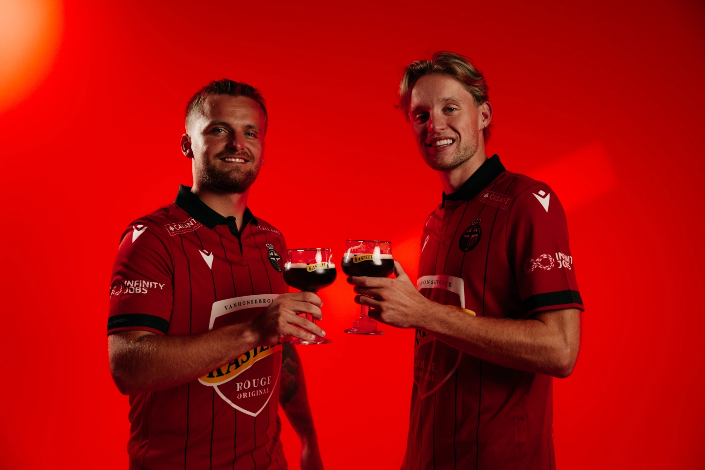 Mandel United uitrusting 2026-2027 met spelers Liam Prez en Jules Desot met elk een glas Kasteel Rouge